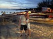 Justin and Pam embracing on a beach in Treasure Beach Jamaica. Sun sets and colorful boats on shore.